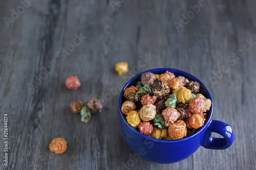 Multicolored sweet popcorn in blue cup on gray wooden background.