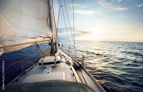 View from a deck of a tilted yacht in strong wind at sunset. Clear sky with glowing golden clouds. Transportation, nautical vessel, cruise, sport, regatta, recreation	