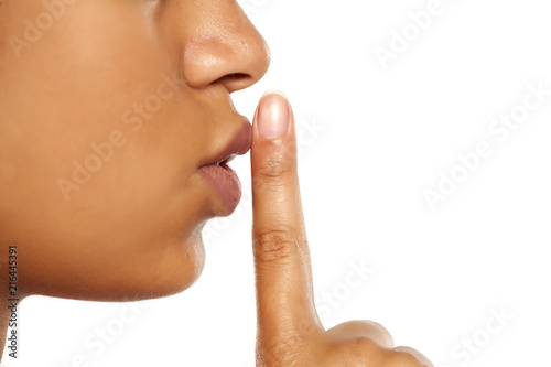 Closeup of a beautiful young dark-skinned woman with finger on her lips on a white background. Concept for silence photo