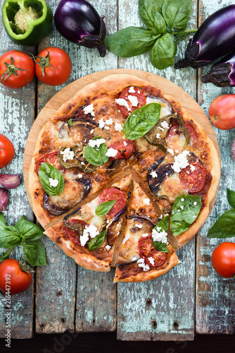 Vegetarian pizza. Aubergine pizza with tomato, bell pepper and basil surrounded with raw ingredients on old shabby blue boards