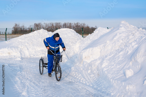 Cyclist in winter on a tricycle on a background of snowy hills, snowdrifts, fences and asphalt.The wheels are slipping.