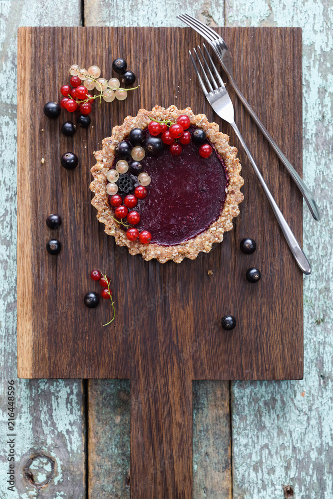 Small vegan tarts made of nuts and berry jam decorated with black, red and white currants on oak cutting board Small vegan tarts made of nuts and berry jam decorated with black, red and white currants on oak cutting board