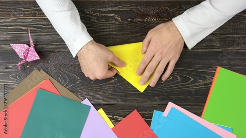 Male hands taking yellow paper. Making triangle with origami paper, top view. photo