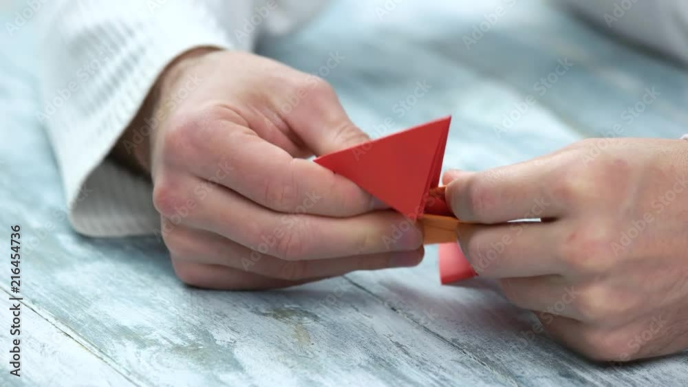 Crafting origami figure with red and orange papers. Male hands making origami, close up. Crafting origami figure with red and orange papers. Male hands making origami, close up.