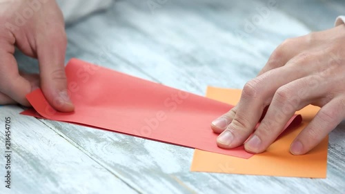 Folding red paper, close up. Male hands making origami, bending and smooting red paper sheet. photo