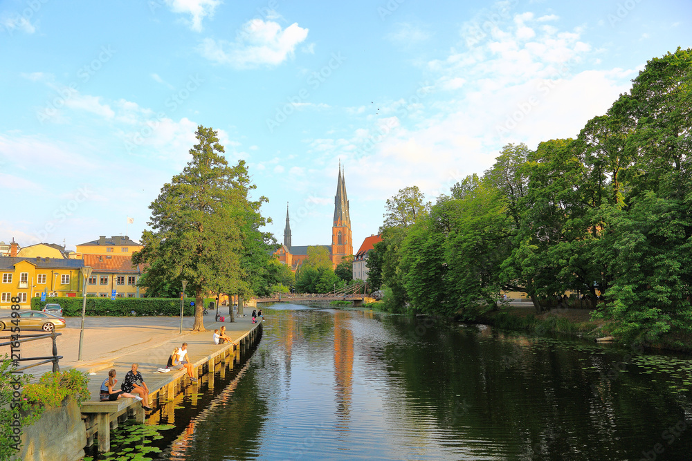 Gorgeous view on street near river with cathedral on background. Gorgeous blue sky with white clouds on a summer day. Tourism / travel concept. Europe, Sweden, Uppsala. 07.27.2018. Gorgeous view on street near river with cathedral on background. Gorgeous blue sky with white clouds on a summer day. Tourism / travel concept. Europe, Sweden, Uppsala. 07.27.2018.
