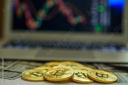 Gold bitcoins and dollar bills appearing from above a laptop with stock exchange charts on the screen