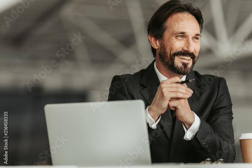 Canvastavla Portrait of smiling bearded businessman holding pen in arms while working with l