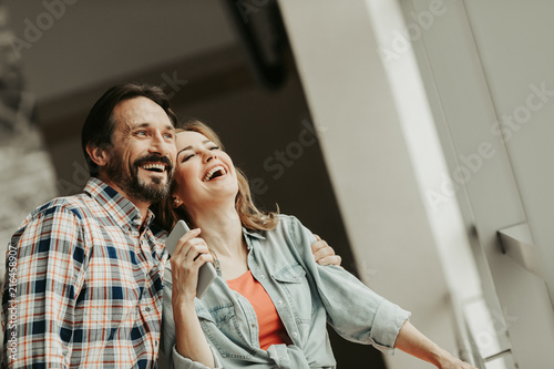Low angle portrait of laughing girl talking with glad bearded male. He hugging her. Love concept