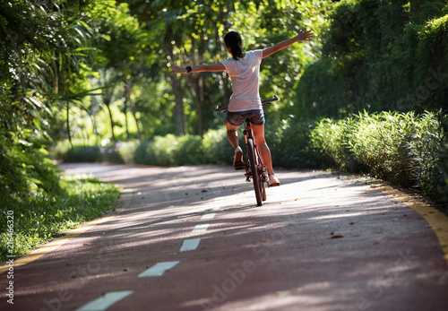 Woman riding a bike on sunny park trail with arms outstretched