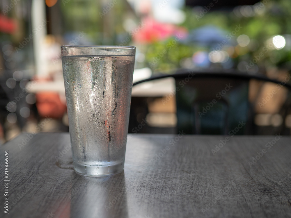 Condensation covered glass of water sitting outside on a dark table 