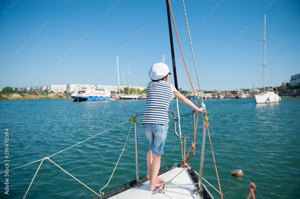 healthy kid in captain hat standing on luxury yacht board in sea port in summer