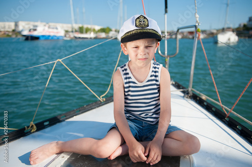 serious kid in captain hat sitting on luxury yacht board in sea port in summer © ruslanshug