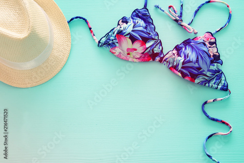 Top view of fashion female swimsuit bikini and white fedora hat over mint wooden background. Summer beach vacation concept.
