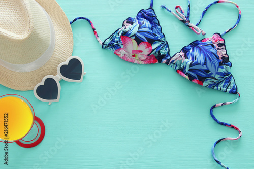 Top view of fashion female swimsuit bikini and white fedora hat over mint wooden background. Summer beach vacation concept.