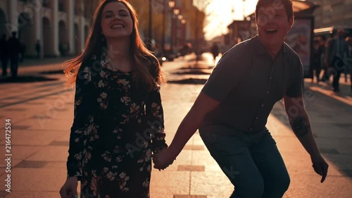 Attractive handsomeyoung couple is jumping down the street and laughing. Slow motion city urban shot. Sunsen or sunrise orange flare. photo