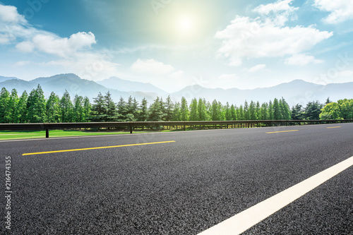 Asphalt road and forest with mountains under the blue sky
