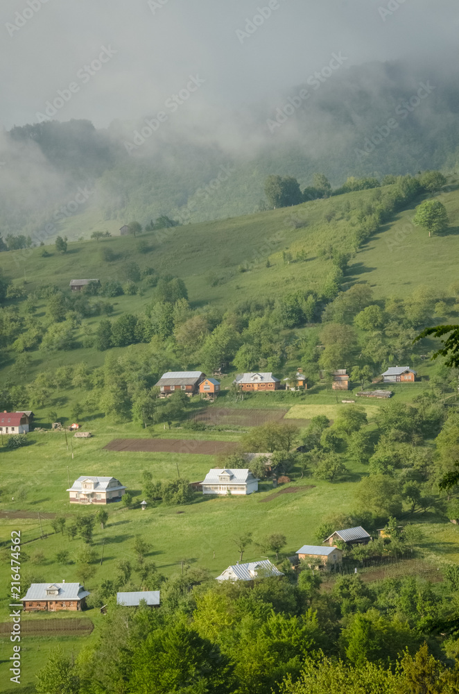 Scenic shot of rural area at mountains taken at sunny spring day. Remote houses are scattered on the slope of the hill covered with forest and meadows. Concept of clear environment. Natural background