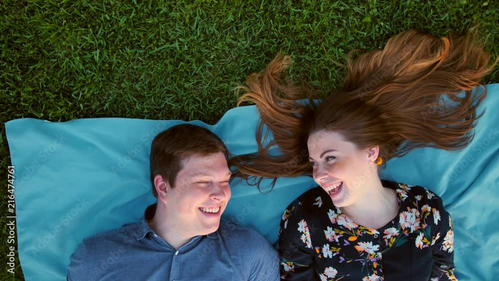 Happy young adult couple lying on the grass over sunset. Vertical camera view in 4k UHD resolution. MAle near female. Woman with freckles and red long hair. Smiling and blowing. Happy young adult couple lying on the grass over sunset. Vertical camera view in 4k UHD resolution. MAle near female. Woman with freckles and red long hair. Smiling and blowing.