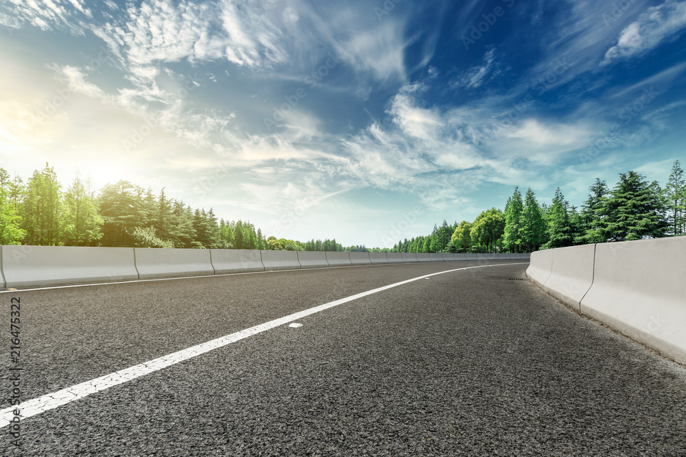 Fototapeta premium Asphalt road and green forest landscape at sunset