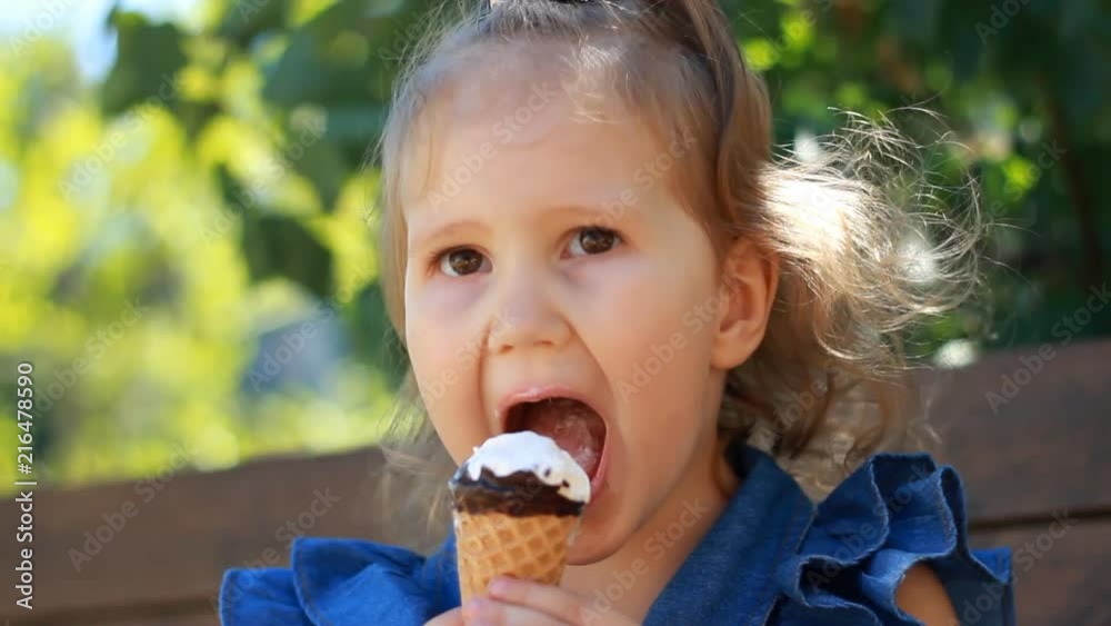 Child girl eats ice cream cone with chocolate In the park on a sunny summer day. Portrait of a baby close-up. Child girl eats ice cream cone with chocolate In the park on a sunny summer day. Portrait of a baby close-up.