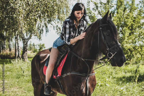 Nice american lady in a plaid shirt and shorts. A beautiful rider and horse. Artistic Photography at horse farm. Attractive girl riding on horse rural location 