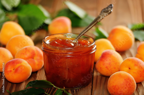 Glass Jar of Apricot jam on wooden table with ripe apricots at background