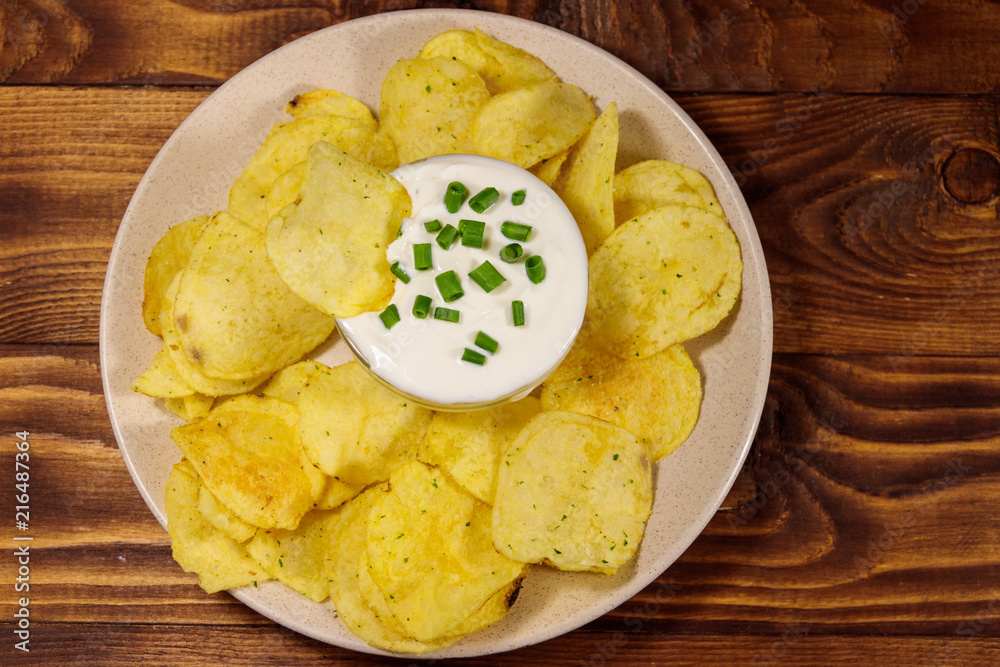 Crispy potato chips with green onion and sour cream on wooden table. Top view Crispy potato chips with green onion and sour cream on wooden table. Top view