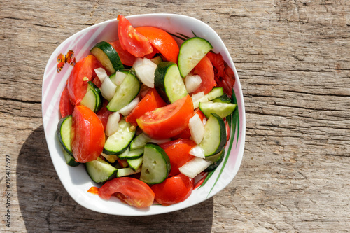 Fresh vegetable salad  with tomatoes, cucumbers, onion and olive oil on wooden table. Top view