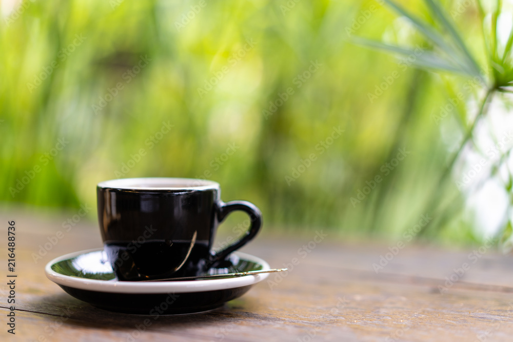 espresso coffee with in the black cup on wooden table with blur tree background espresso coffee with in the black cup on wooden table with blur tree background