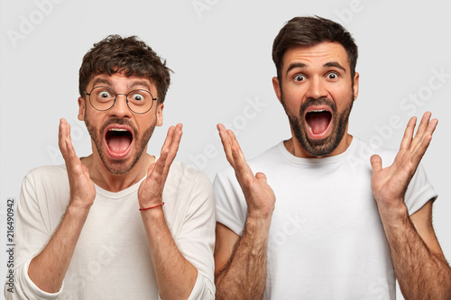 Astonished amazed joyful two men exclaim with surprisement, gesture actively, keep jaws dropped, can`t believe in such success, dressed casually, isolated over white background. Body language concept