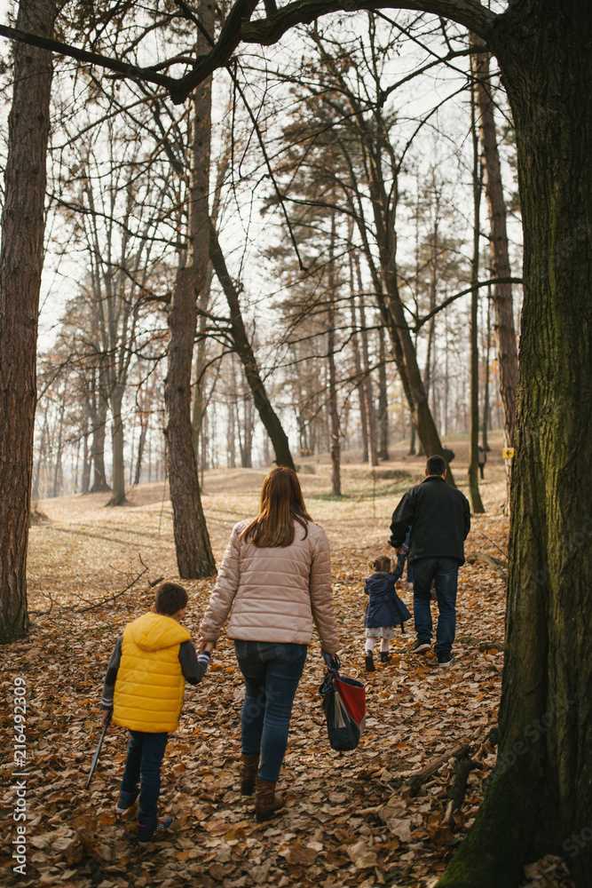 Fototapeta premium Happy young family enjoying in beautiful autumn day in park. They are smiling and walking on sunset.