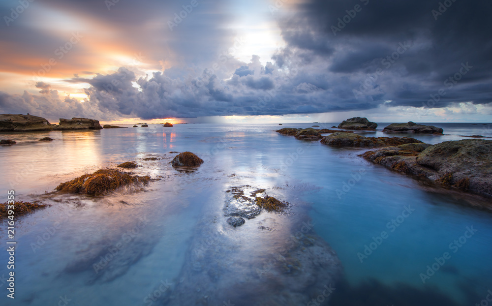 colorful sunset seascape with natural coastal rocks on the ground. soft focus due to slow shutter and water movement.