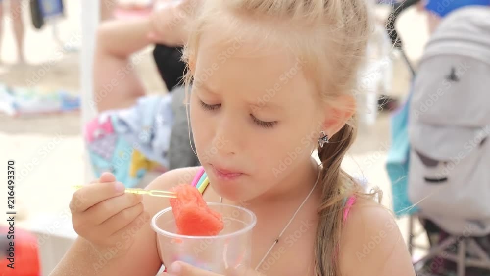 Happy little girl eating watermelon slices on the beach. Summer holiday picnic outdoors. Happy little girl eating watermelon slices on the beach. Summer holiday picnic outdoors.