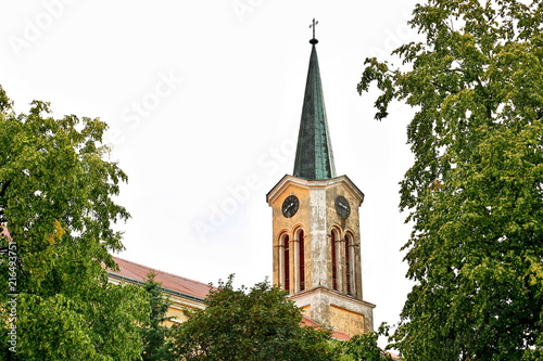 Church tower with green roof and a metal cross on the top, yellow and white paint-peeled facade, red roof, historical architecture, old clock, Saint Thomas in Hudlice, Czech Republic, Europe