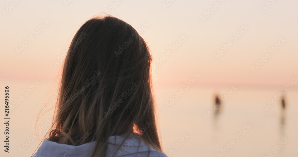 teenage girl standing on a beach at sunset shot from behind teenage girl standing on a beach at sunset shot from behind