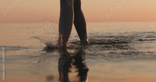 closeup young female legs walking in shallow water on a beach
