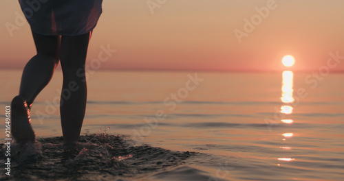 closeup young female legs walking in shallow water on a beach