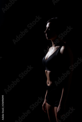A sports girl in black shorts and a topic is standing on a black isolated background. Female portrait in a low key. © pushann