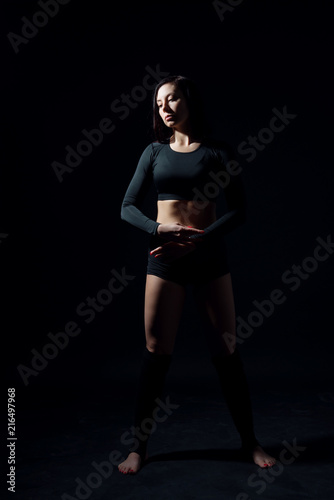 Sports girl in black top and shorts in a dance position on a black isolated background. Female portrait in a low key.