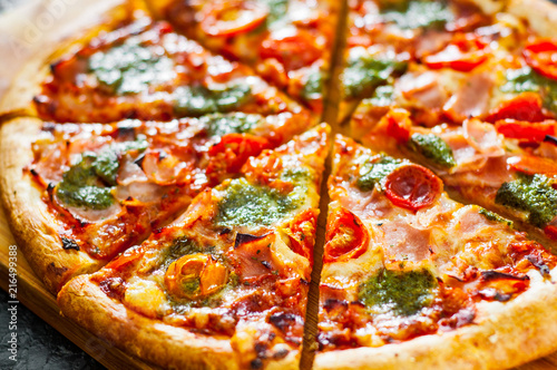 sliced Pizza with Mozzarella cheese, Ham, Tomatoes, pepper, Spices and Fresh Basil pesto sauce. Italian pizza.