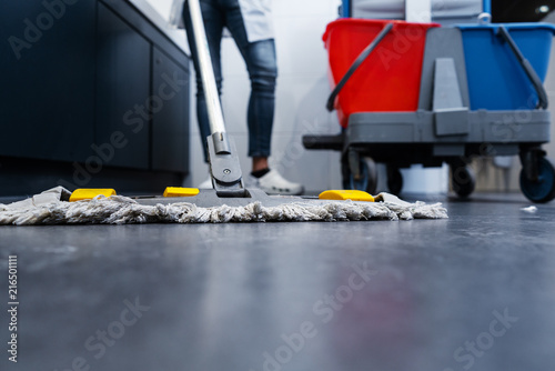 Foto Low shot of cleaning lady mopping the floor in restroom beside her trolley