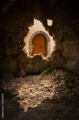 An old wooden arched door in Sicily seen through a broken hole in a stone wall