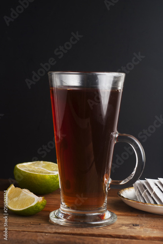 Glass Cup ofblack tea with lime, close up on rustic wooden background. Warm autumn or winter drinks.