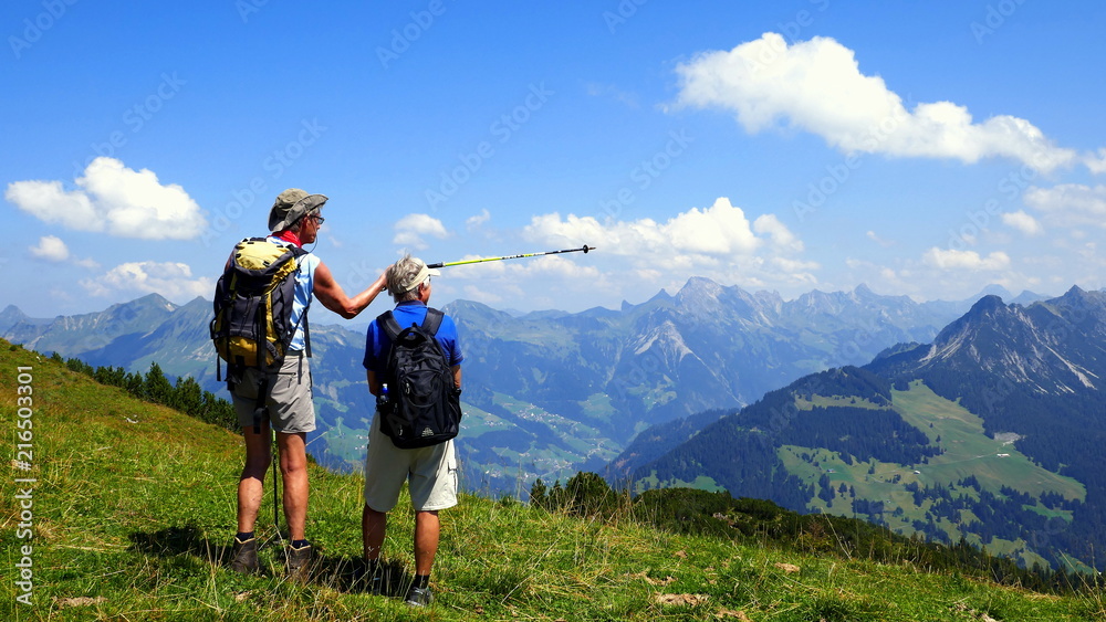 2 Wanderer betrachten vom Hohen Frassen aus die herrliche Bergkette im sonnigen Bregenzerwald 