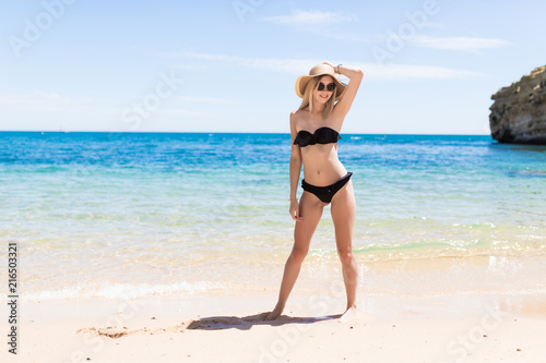 Happy woman in bikini and sunhat in sunglasses on sea beach