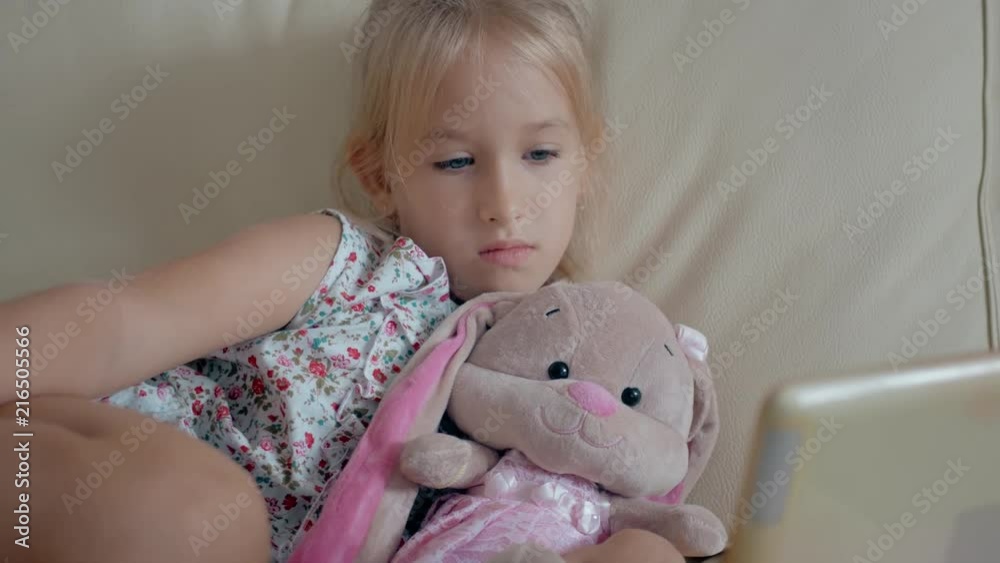 Cute girl and her favorite toy is a plush rabbit with tablet computer at home.