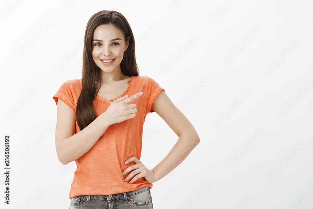 Suggesting us go with her. Portrait of attractive slender european female model with confident expression, holding hand on hip and pointing right with broad smile, asurring it is good choice
