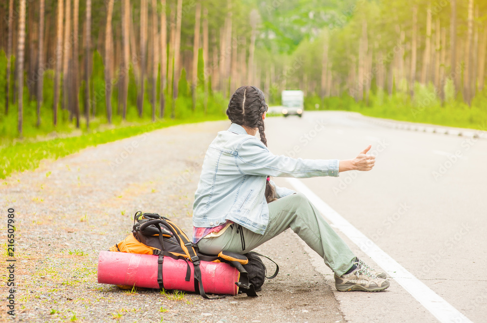 woman sitting on a backpack and hitchhiking on the road woman sitting on a backpack and hitchhiking on the road