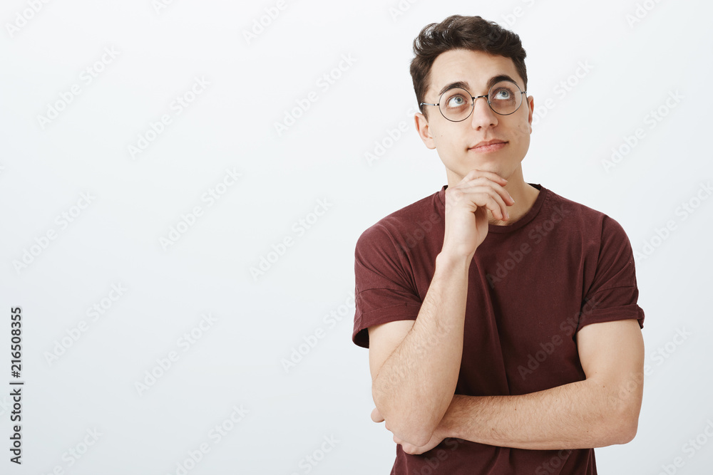 Portrait of dreamy creative businessman in red t-shirt and round glasses, holding hand on chin, looking upwards with slight pleased smile, enjoying nice view or thinking about pleasant memories Portrait of dreamy creative businessman in red t-shirt and round glasses, holding hand on chin, looking upwards with slight pleased smile, enjoying nice view or thinking about pleasant memories